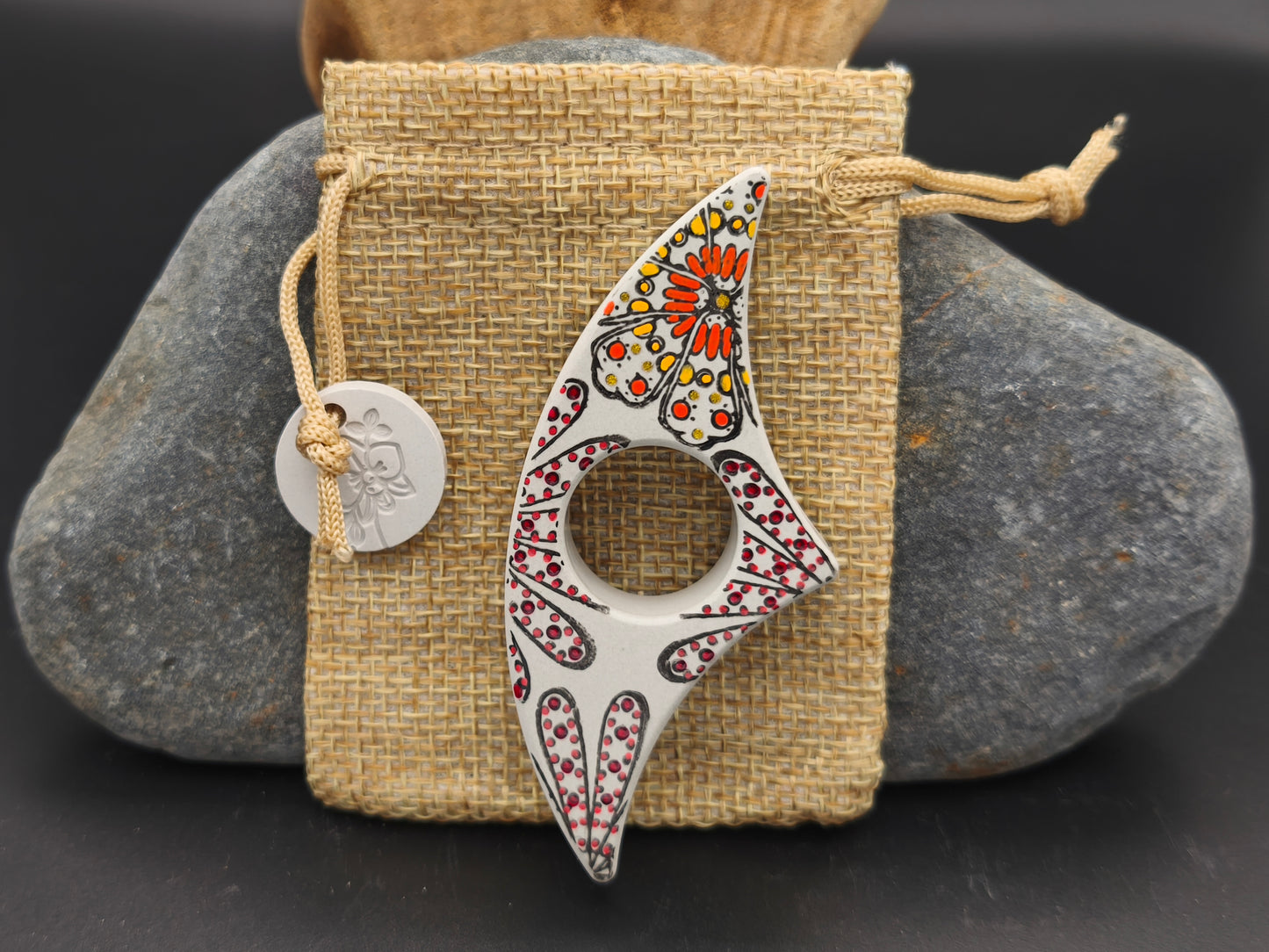 Bague de lecture artisanale gris cendré décorée de fleurs de feu orangées, présentée sur un pochon en toile de jute – création Omiralys.