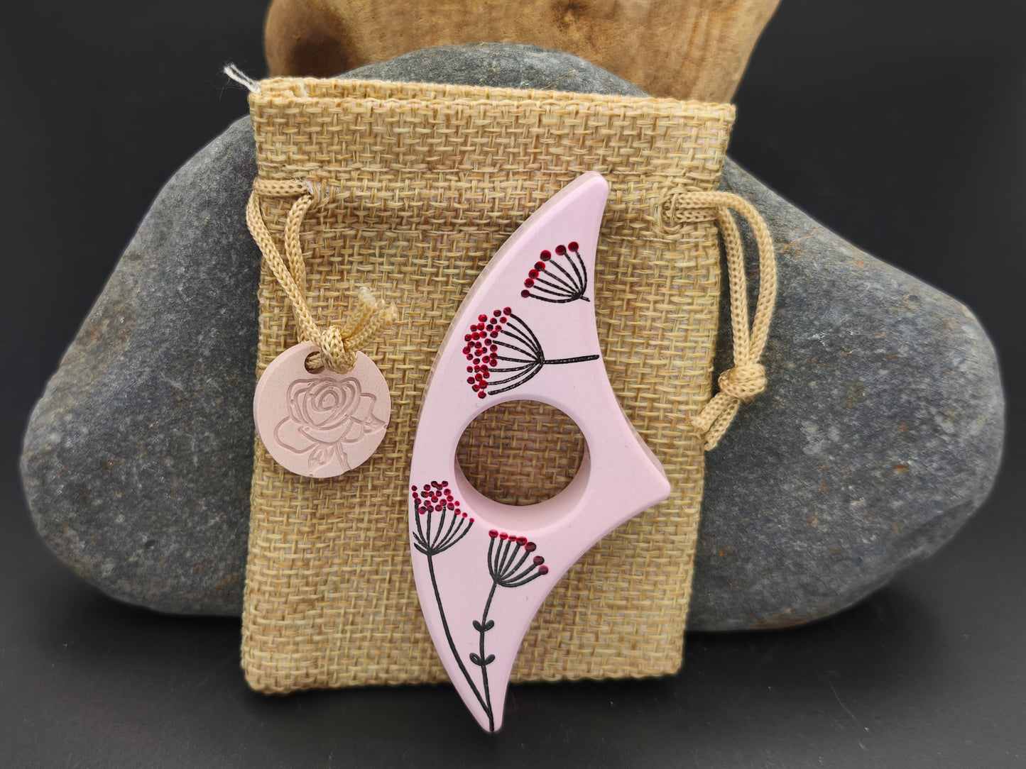 Bague de lecture artisanale Omiralys rose floral et graines poétiques présentée sur son pochon en toile de jute avec sa médaille assortie.