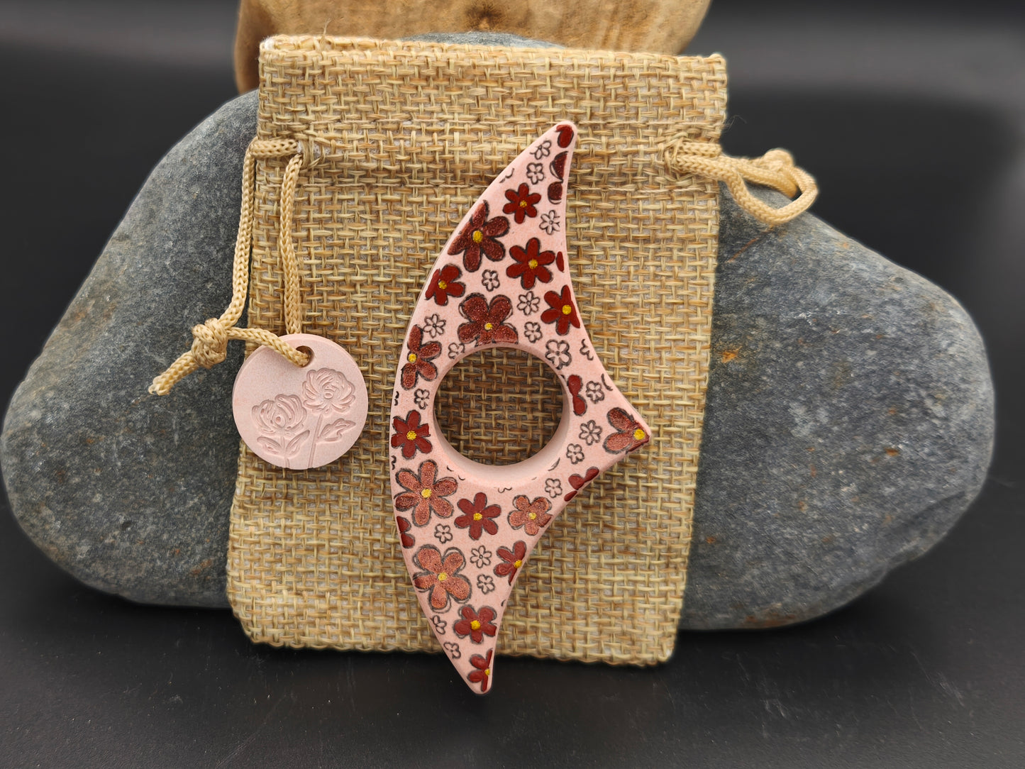 Bague de lecture artisanale rose poudré décorée de fleurs rouges, orangées et dorées, présentée sur un pochon en toile de jute – création Omiralys.