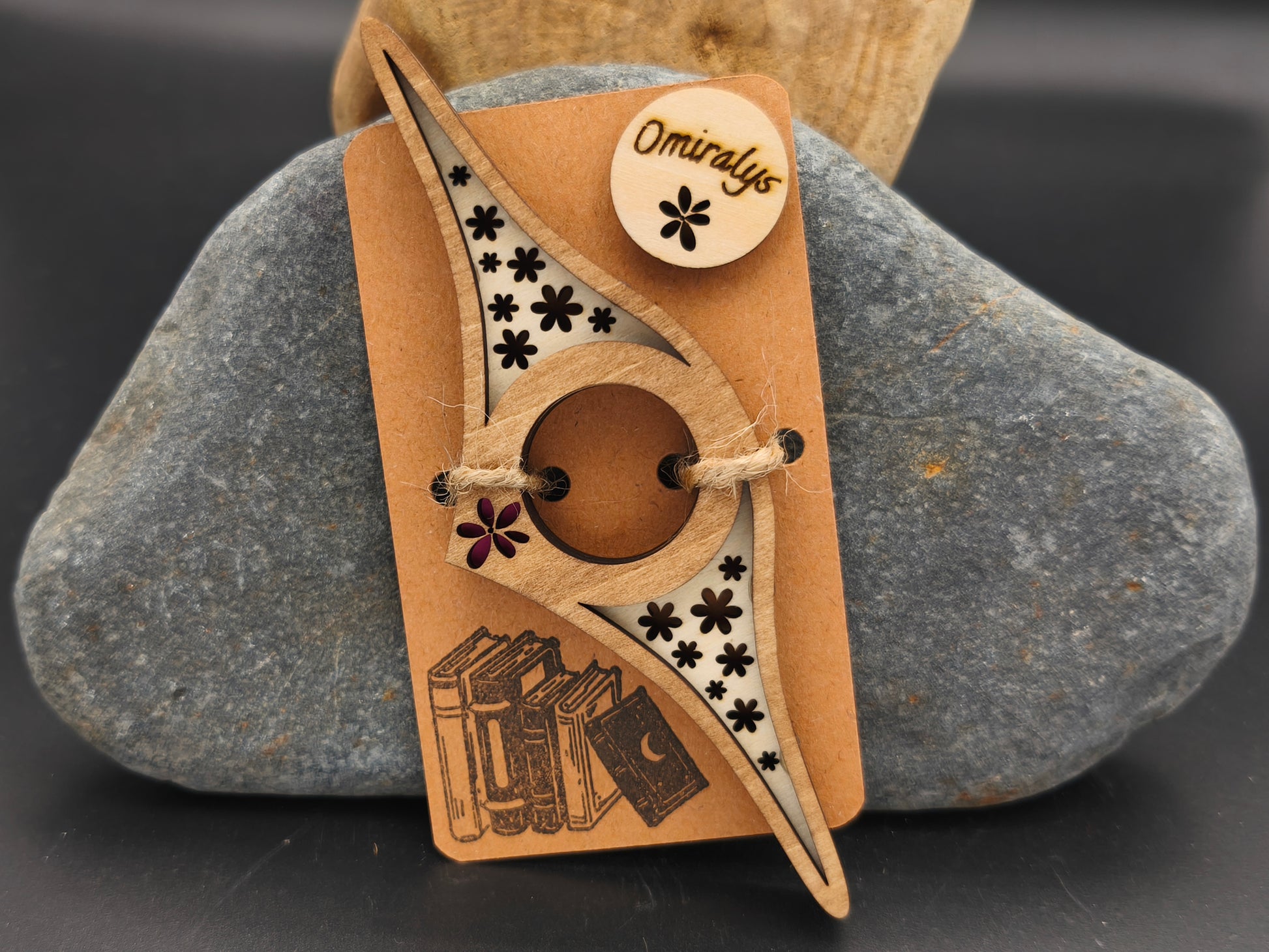 Bague de lecture artisanale Omiralys en bois de tilleul bicolore avec constellation de fleurs évidées et petite fleur rouge en relief 3D sur support kraft.