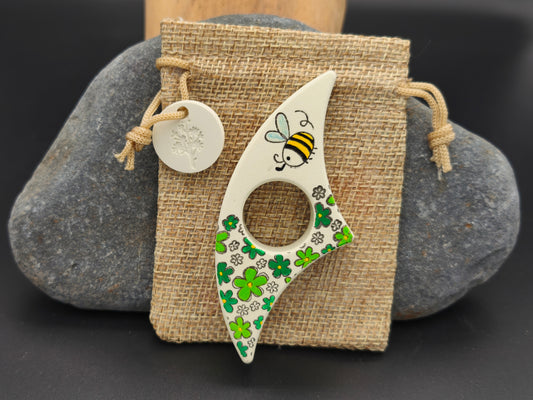 Bague de lecture artisanale Omiralys vert pastel avec décor abeille et trèfles sur son pochon en toile de jute.