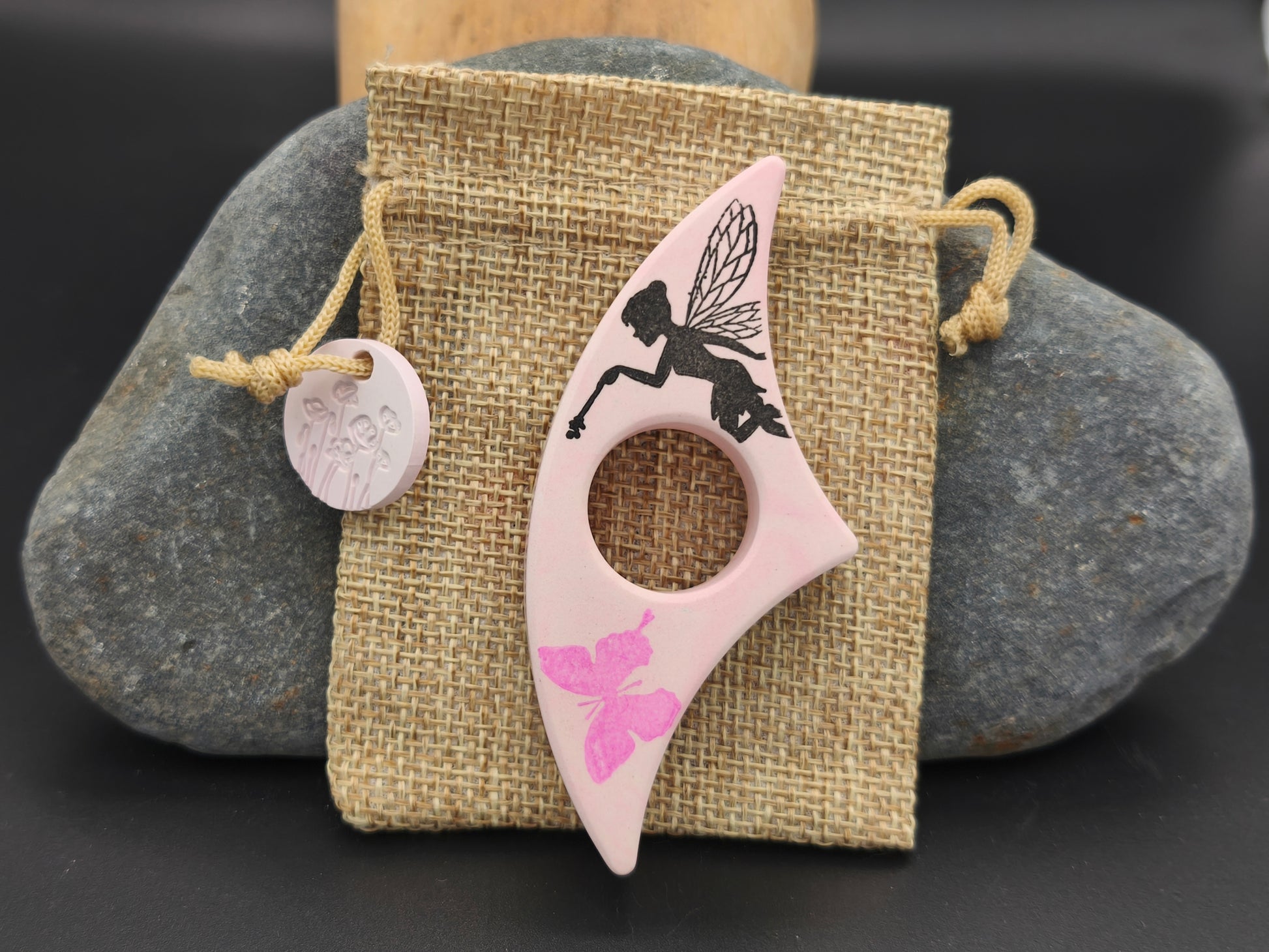 Bague de lecture artisanale Omiralys rose clair avec fée noire et papillon rose vif sur son pochon en toile de jute.