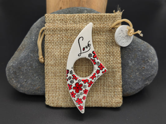Bague de lecture artisanale Omiralys blanche avec fleurs rouges, noires et inscription Love sur son pochon en toile de jute.