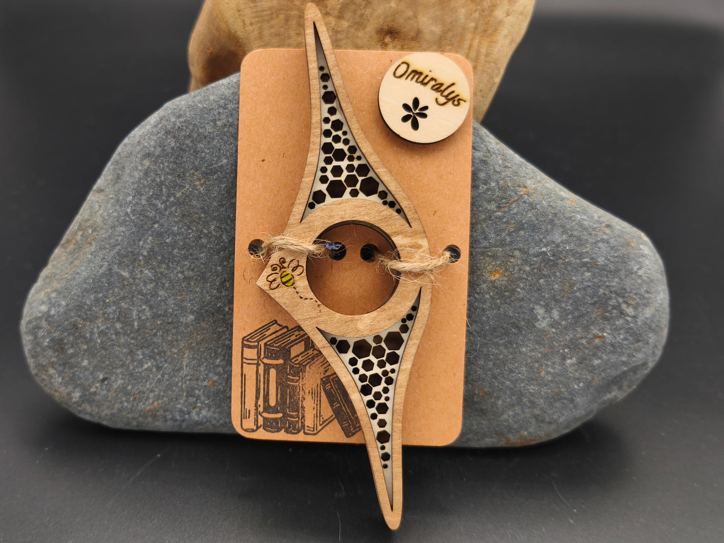 Bague de lecture artisanale Omiralys en bois de tilleul avec motif nid d'abeille ajouré et petite abeille jaune gravée en bas sur support kraft.