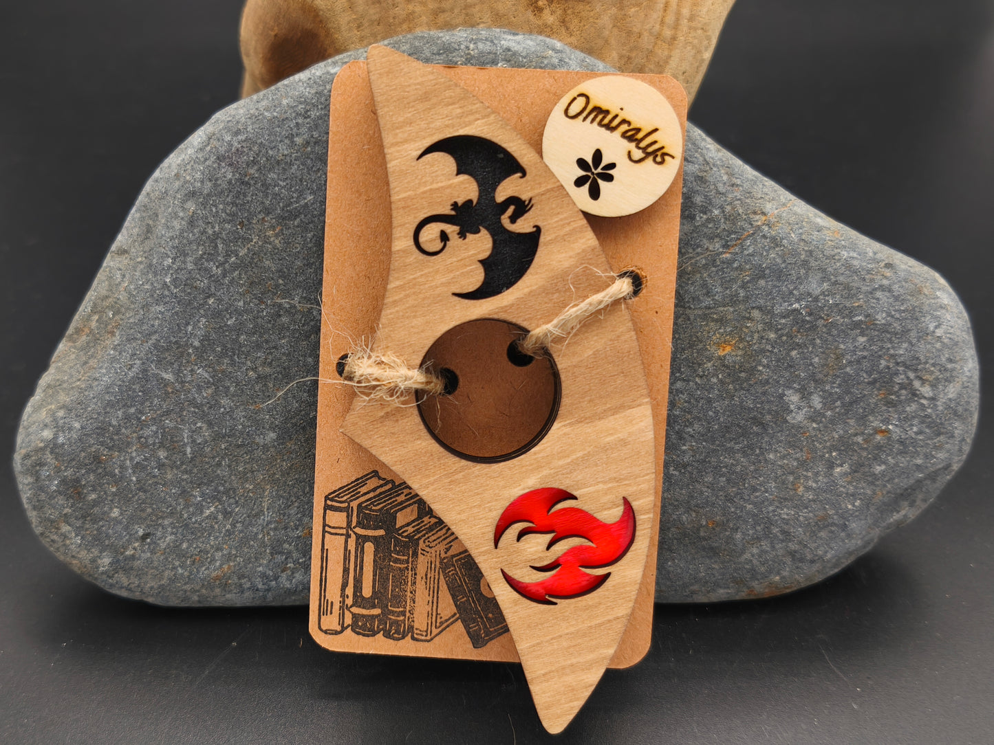 Bague de lecture artisanale Omiralys en bois de tilleul avec silhouette de dragon noir et flamme rouge en relief 3D sur support kraft.