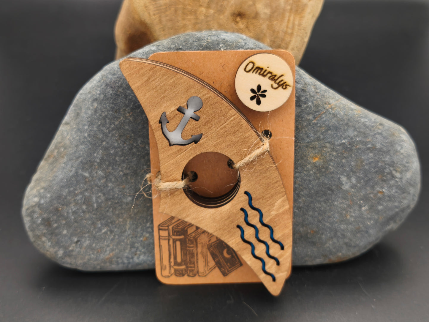 Bague de lecture artisanale Omiralys en bois de tilleul avec ancre noire et vagues bleues en relief 3D sur support kraft.