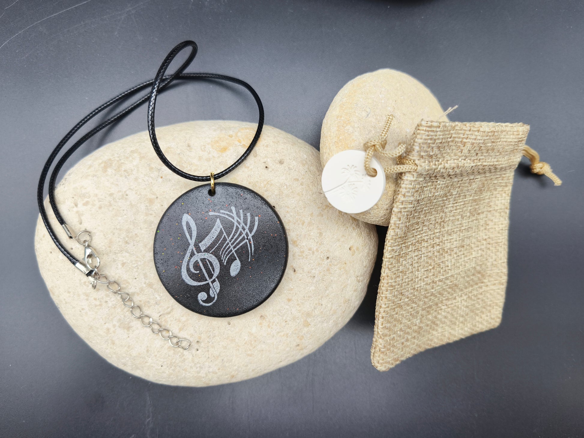 Collier unique Omiralys modèle Ebonique avec pendentif rond noir, clé de sol blanche et reflets pailletés.
