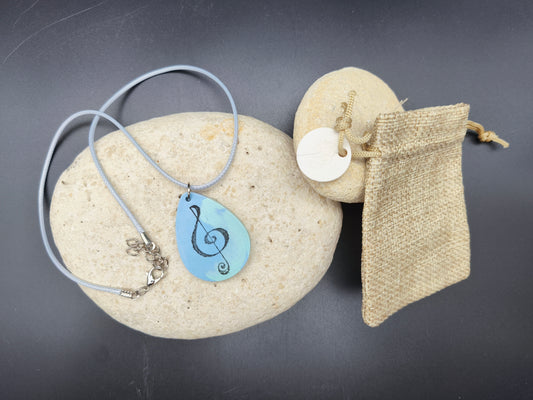 Collier unique Omiralys modèle Solcéleste avec pendentif goutte bleu, motif clé de sol noire sur cordon bleu réglable.

