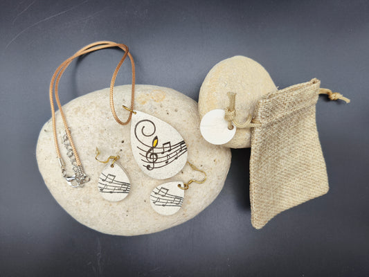 Parure de bijoux unique Omiralys modèle Portelodie avec collier goutte et boucles d'oreilles motif portée musicale sur blanc pailleté.