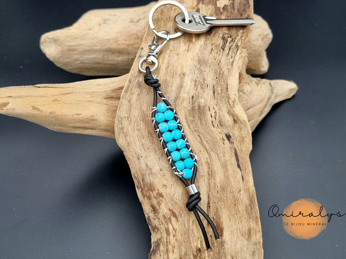 Porte-clés en cuir howlite turquoise posé sur un morceau de bois flotté.