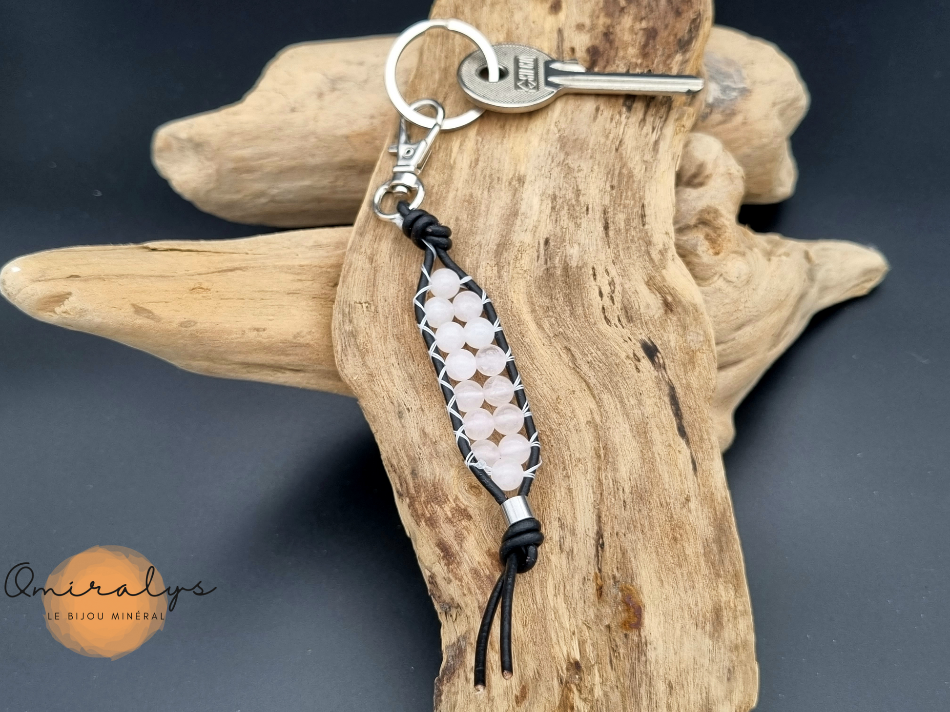 Porte-clés en cuir quartz rose posé sur un morceau de bois flotté.