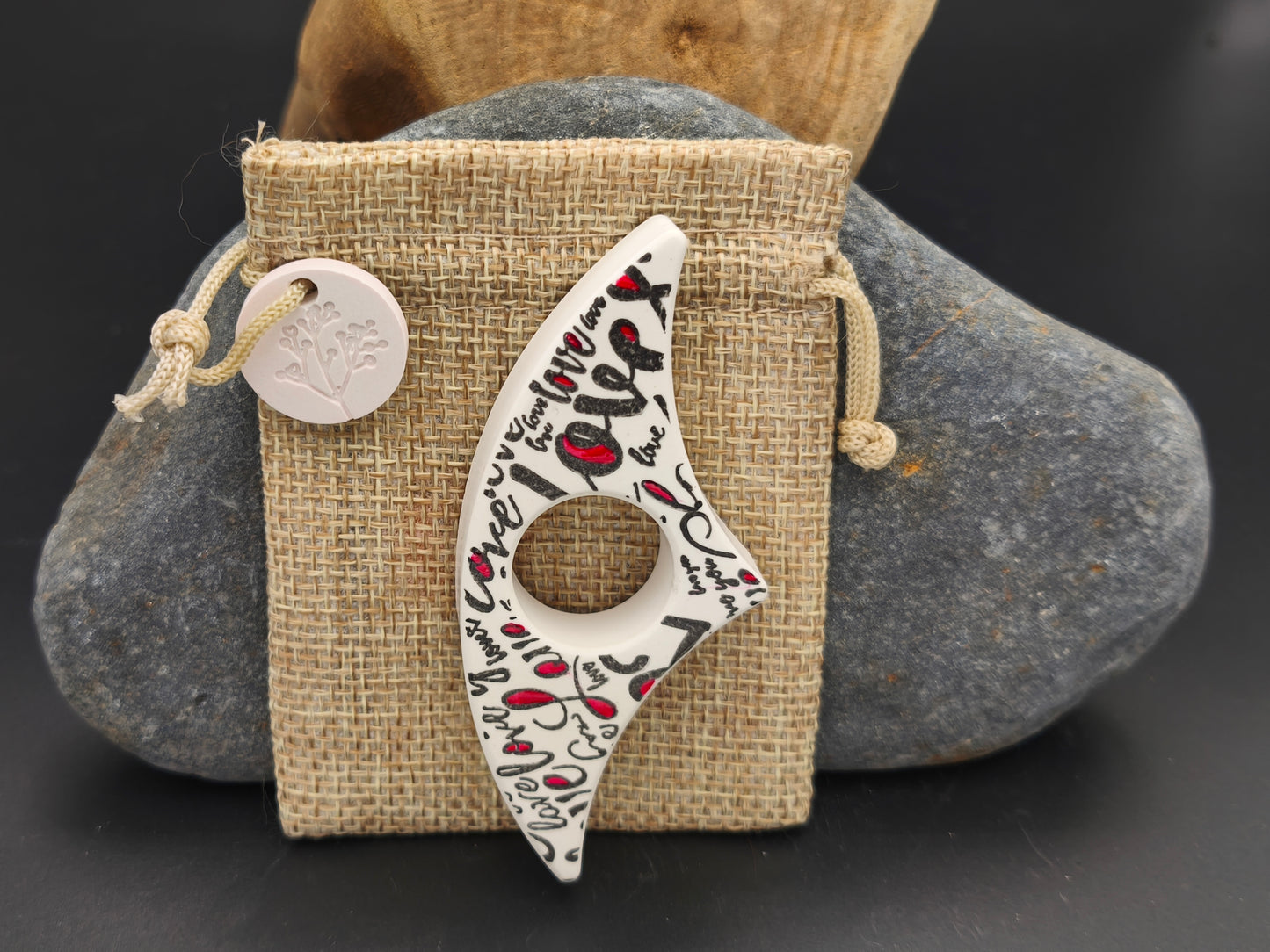 Bague de lecture artisanale blanche décorée d’écritures poétiques noires, présentée sur un pochon en toile de jute – création Omiralys.