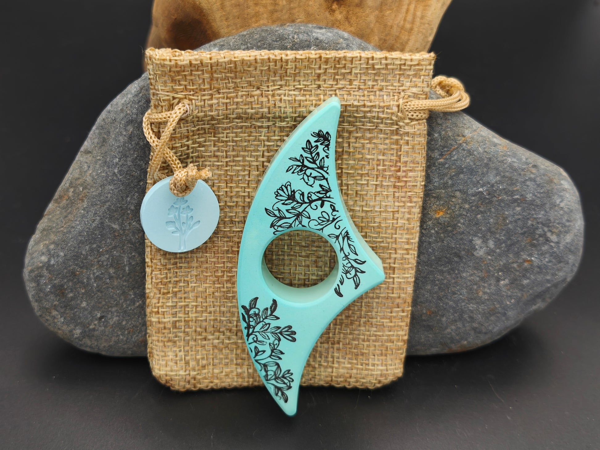 Bague de lecture artisanale Omiralys bleu végétal avec décor feuillage noir sur son pochon en toile de jute et médaille assortie.
