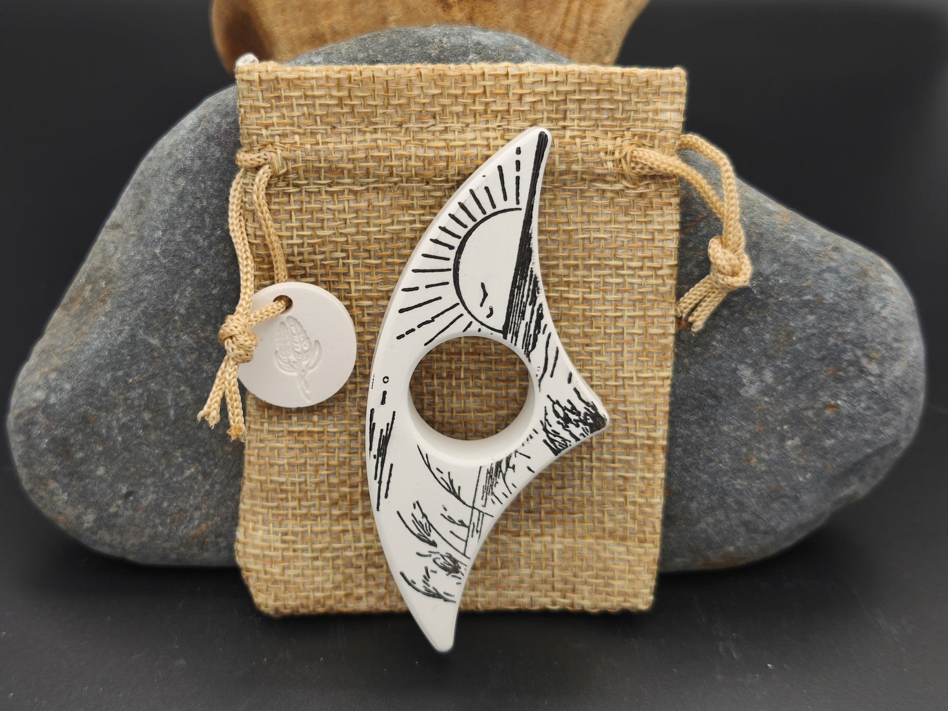 Bague de lecture artisanale noir et ivoire décorée d’un soleil levant minimaliste, présentée sur un pochon en toile de jute – création Omiralys.