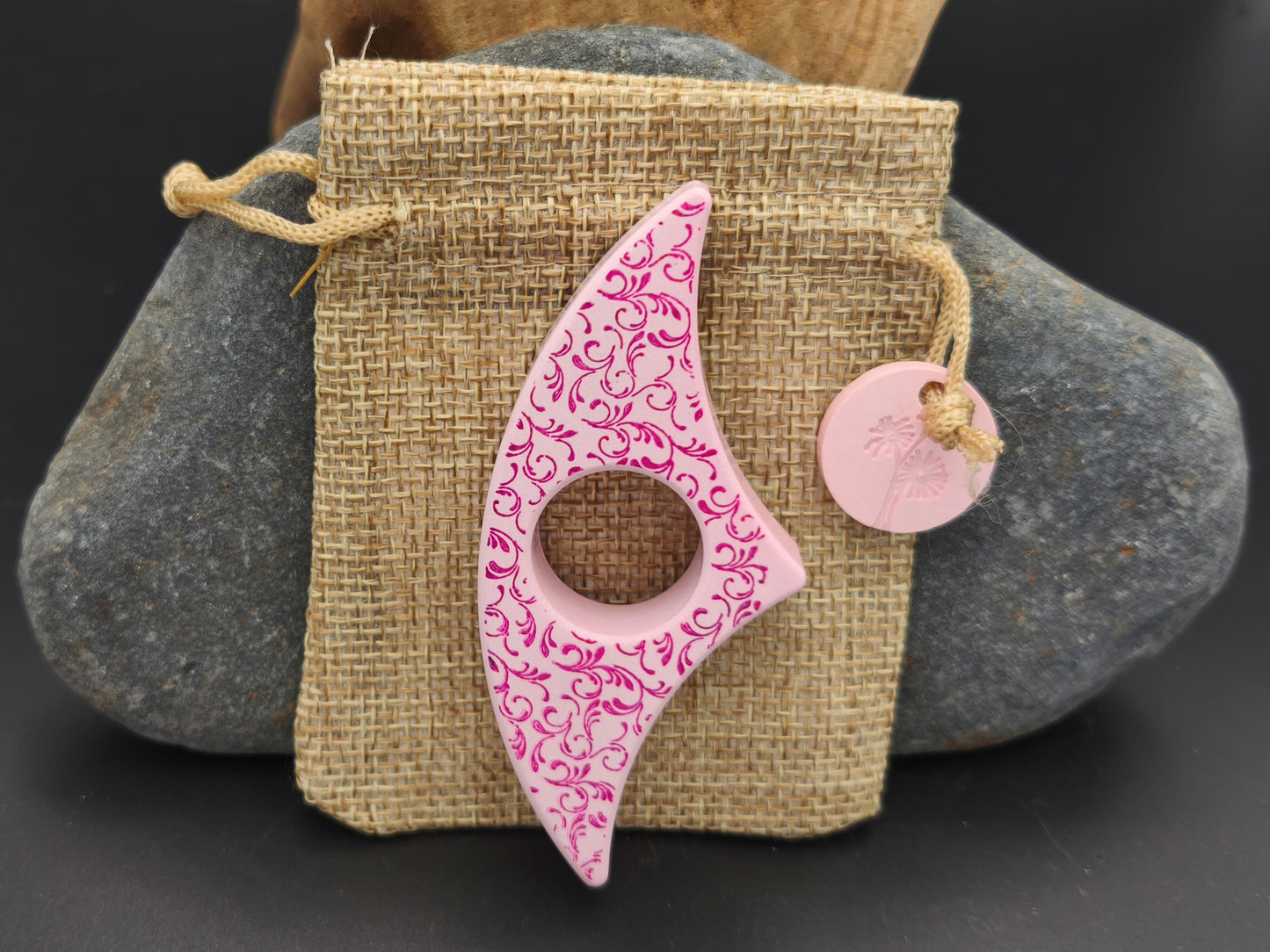 Bague de lecture artisanale Omiralys rose tendre avec arabesques fuchsia sur son pochon en toile de jute et médaille rose assortie.