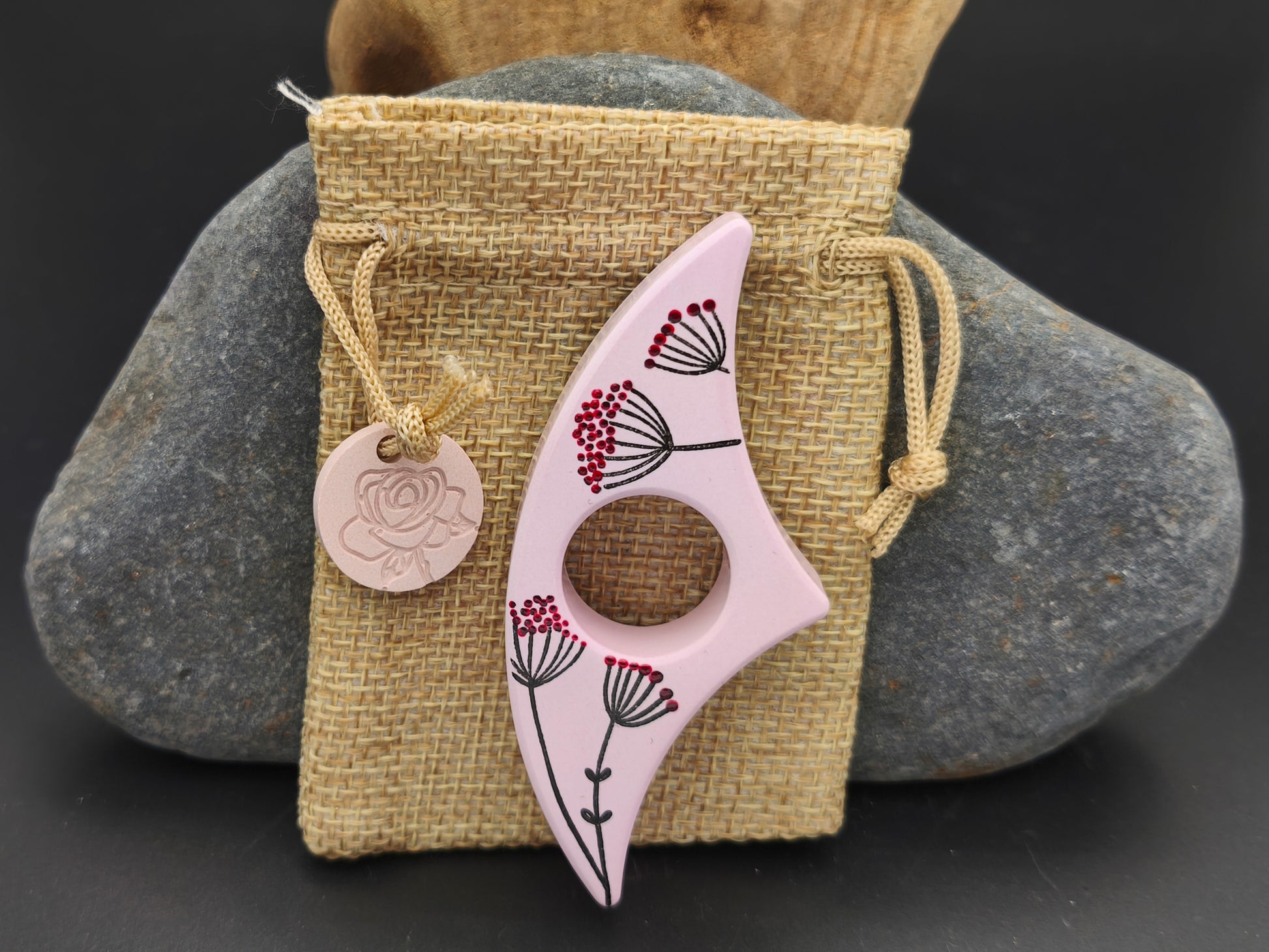 Bague de lecture artisanale Omiralys rose floral et graines poétiques présentée sur son pochon en toile de jute avec sa médaille assortie.