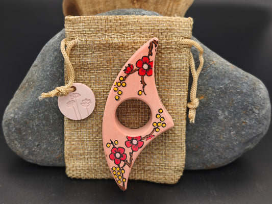 Bague de lecture artisanale rose pêche décorée de fleurs rouges et jaunes, présentée sur un pochon en toile de jute – création Omiralys.